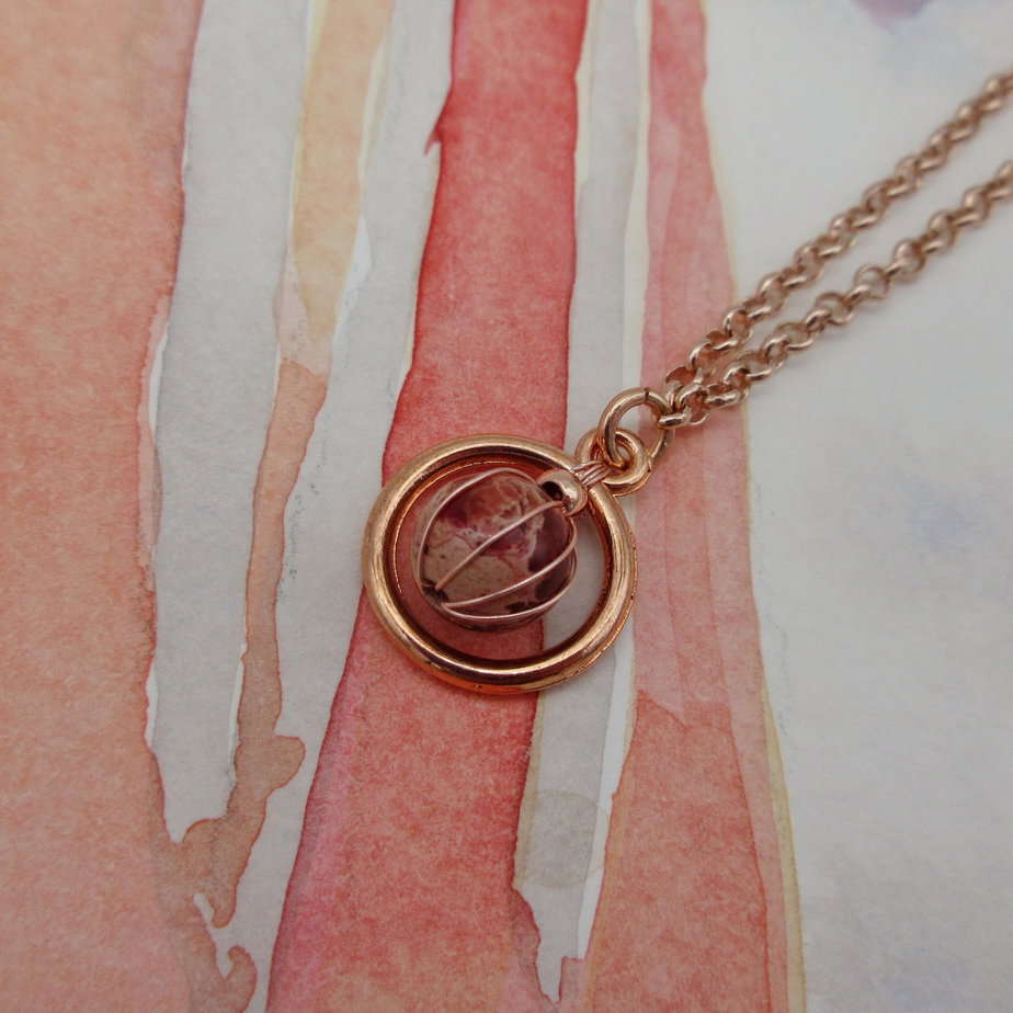 Red jasper round gemstone set inside rose gold plated circular frame on rose gold plated chain.