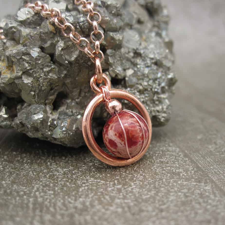 Rose gold plated circular pendant with red jasper gemstone in centre. On rose gold plated chain.