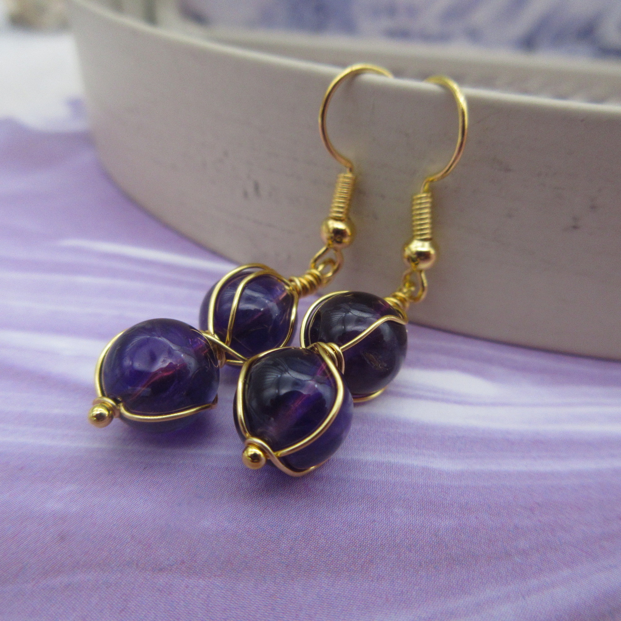 Drop earrings with two deep purple amethyst spheres twisted with gold coloured wire. On gold-plated ear wires.