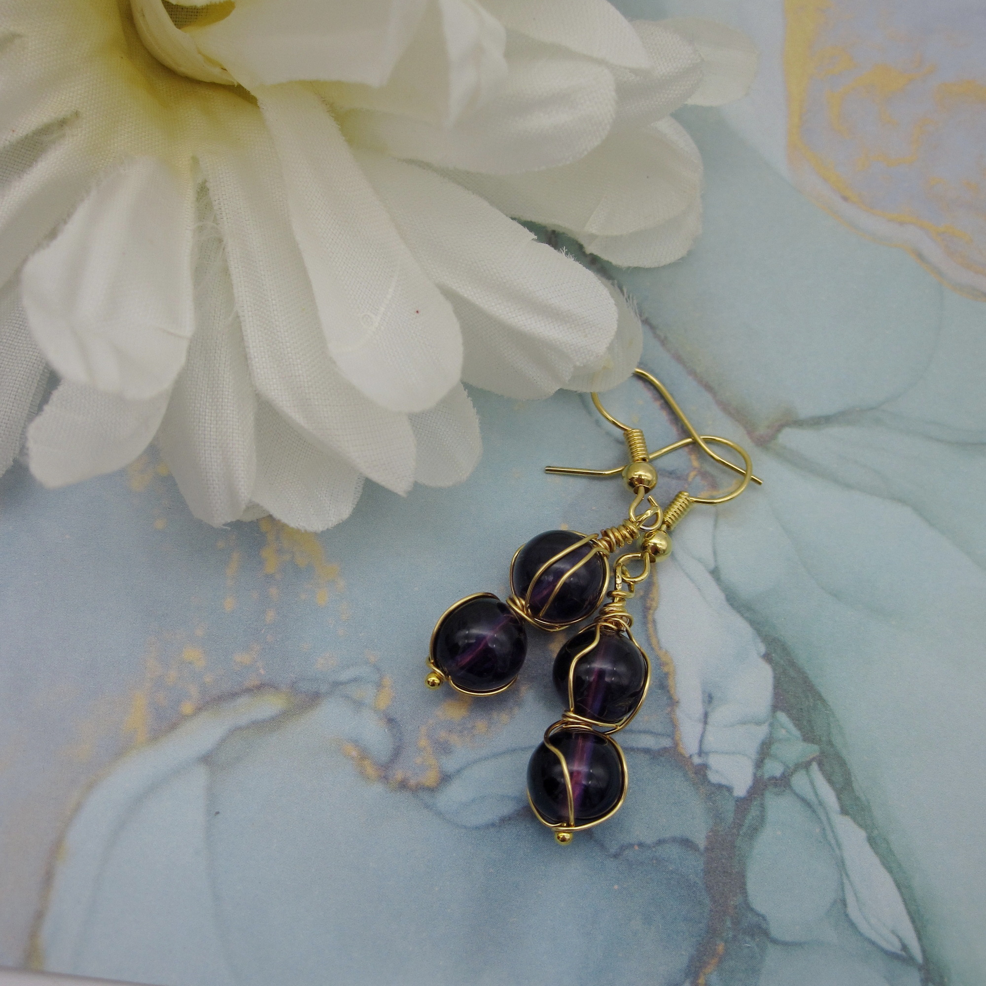 Drop earrings with two deep purple amethyst spheres twisted with gold coloured wire. On gold-plated ear wires.