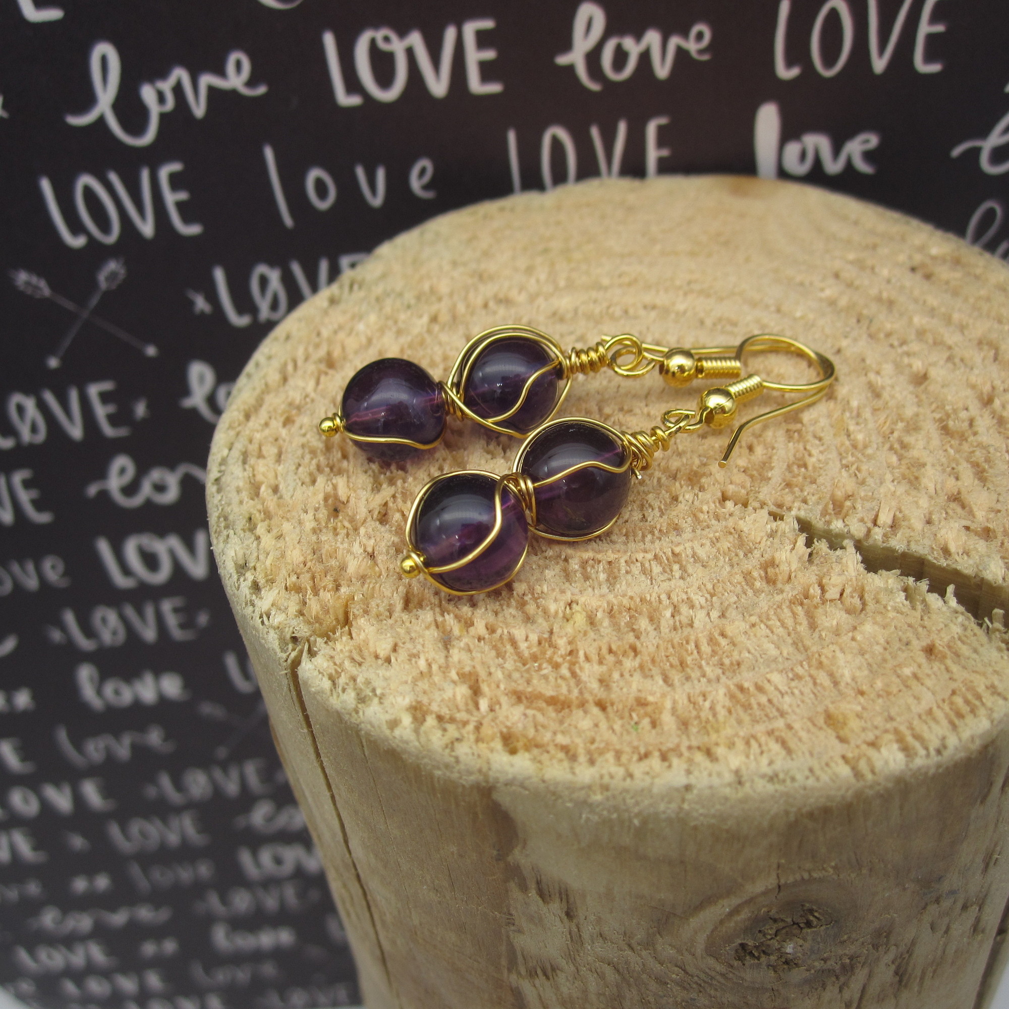 Drop earrings with two deep purple amethyst spheres twisted with gold coloured wire. On gold-plated ear wires.
