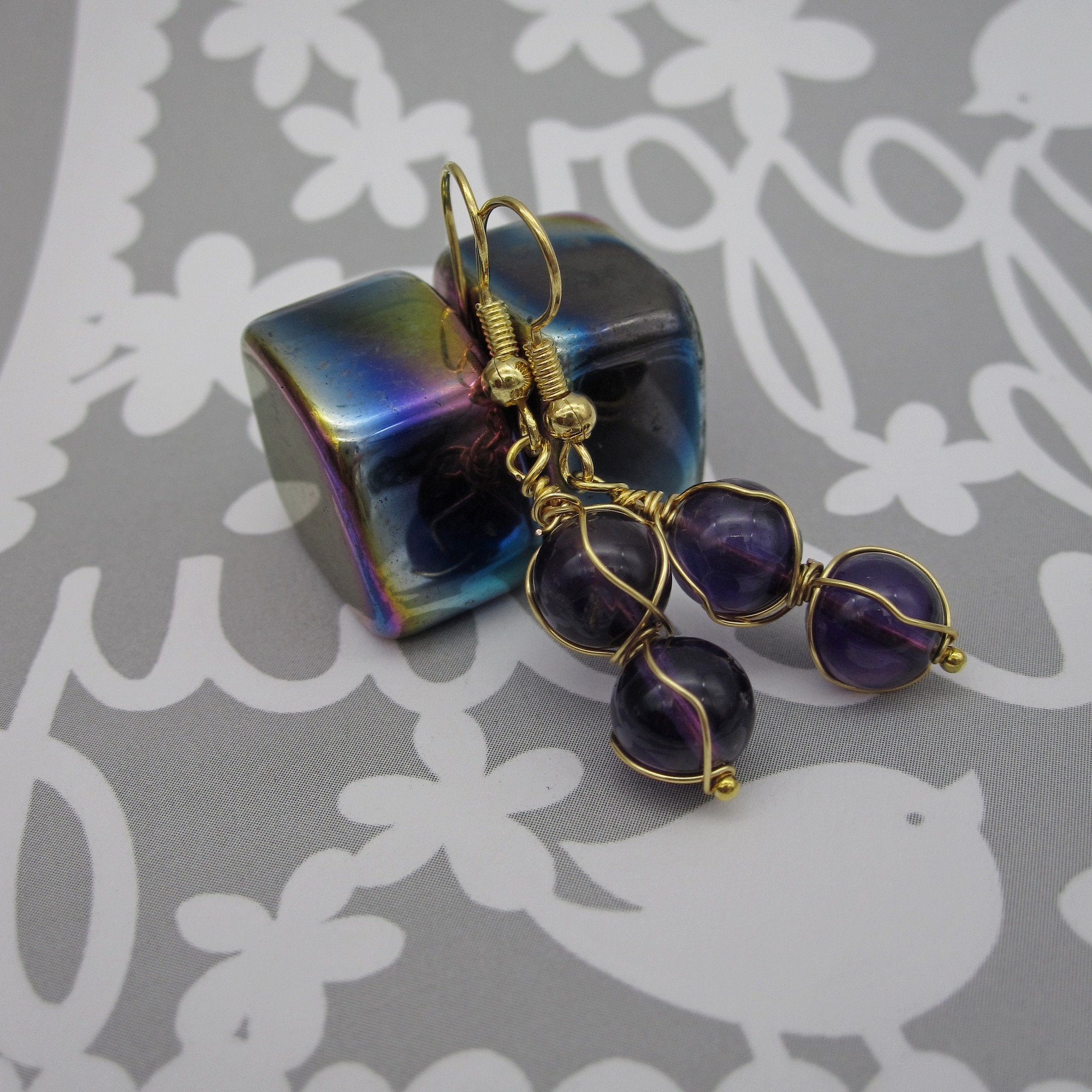 Drop earrings with two deep purple amethyst spheres twisted with gold coloured wire. On gold-plated ear wires.